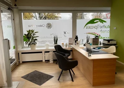 Empfangsbereich mit Schreibtisch, Stühlen und Fensterfront der Naturheilpraxis Gransch